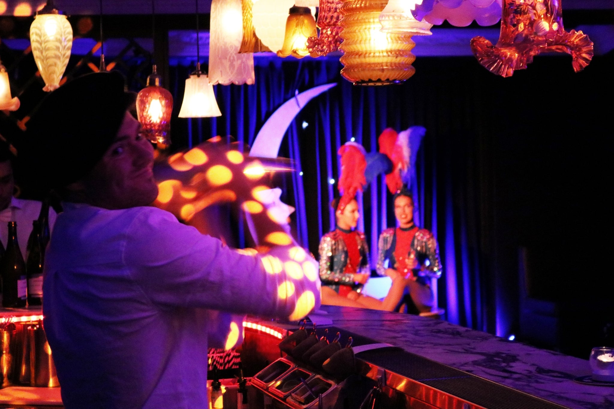 Burlesque cabaret bar in Kings Cross with bartender mixing cocktails and French showgirls seated in background.