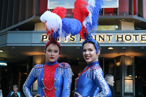 The Honeycomb Club is the place to see a traditional cabaret dinner show. Two showgirls from the Honeycomb Club, wearing feathered headpieces, stand in front of a the well-known Potts Point Hotel in Kings Cross.